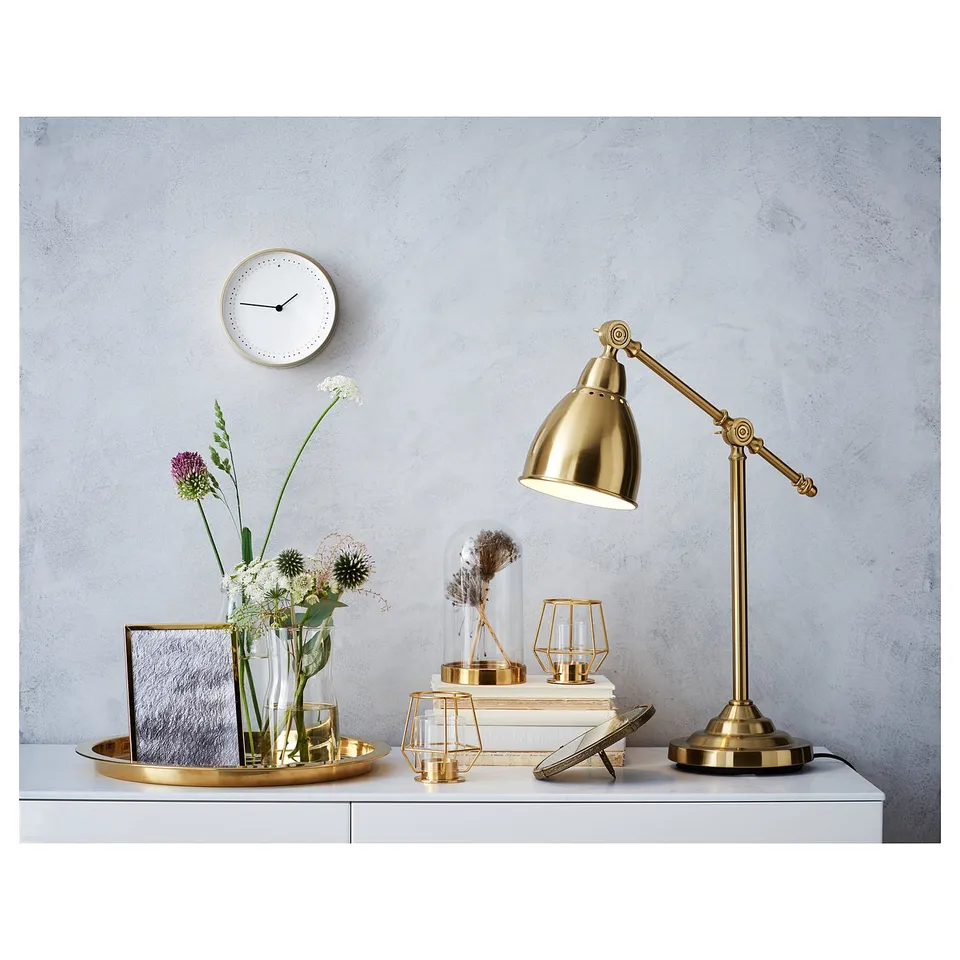 Luxury gold desk setup: brass lamp, candles, flowers, clock.
