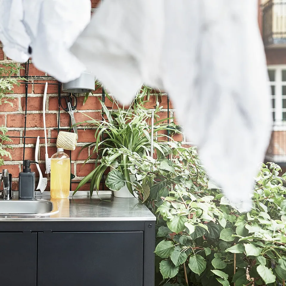 Small outdoor sink, sleek stainless steel, set against brick wall, surrounded by plants, hanging towels, practical design.