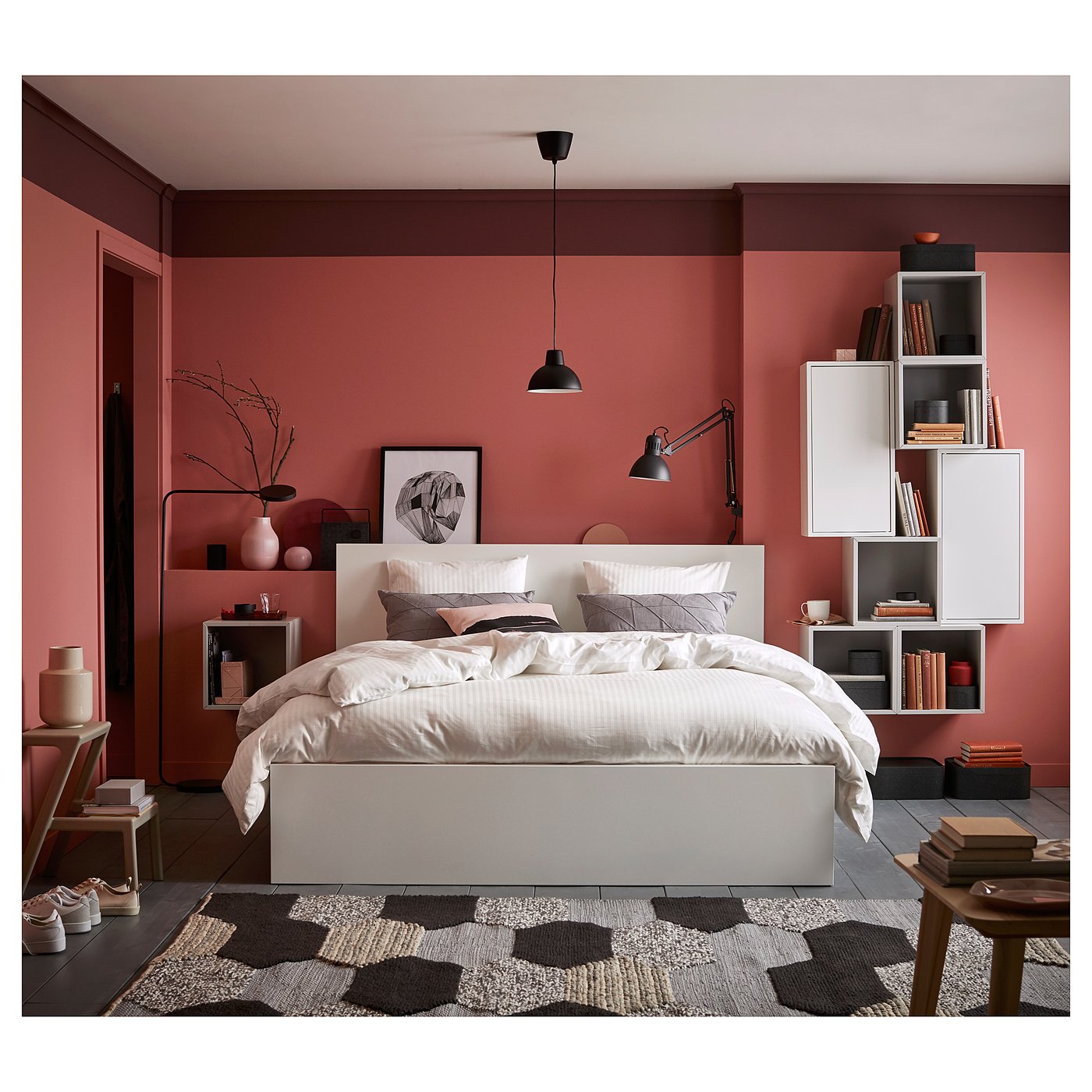 Stylish modern bedroom with red walls, white MALM bed with drawers, geometric rug, hanging light, and wall shelves with books and decor.