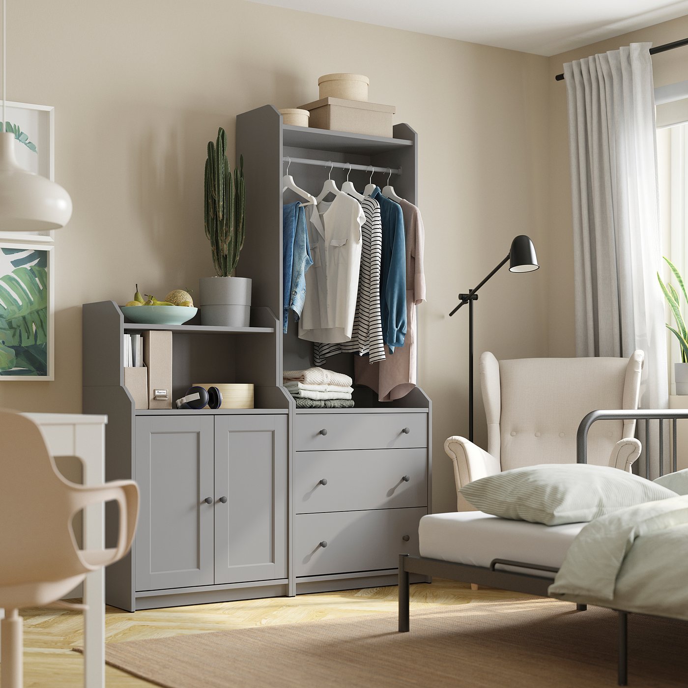 Beautiful bedroom with HAUGA grey storage unit, white curtains, and cosy chair. Clothes hang neatly, decor includes a cactus.