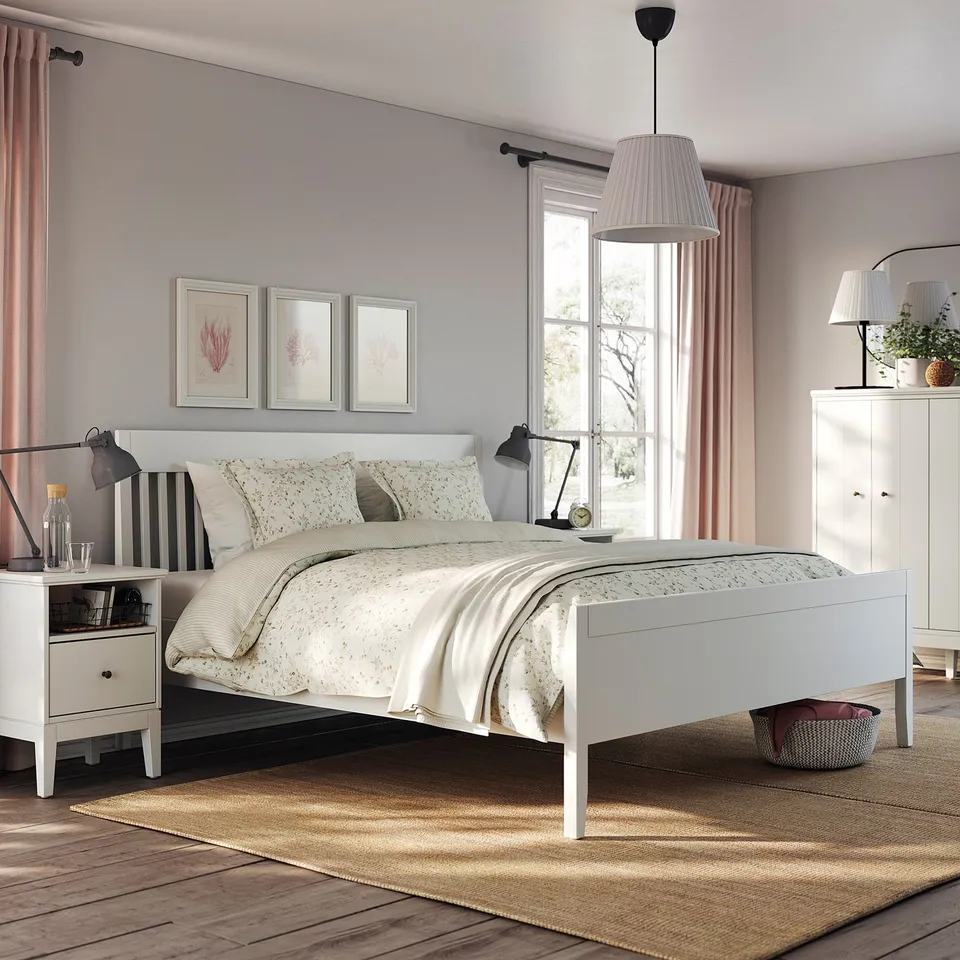 Modern bedroom with white IDANÄS bed, light grey walls, floral bedding, black lamps, and natural rug.