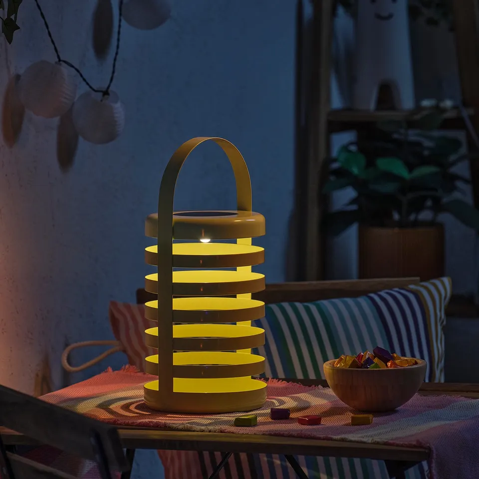Unique lamp on patio table glowing with soft light, surrounded by colourful objects.