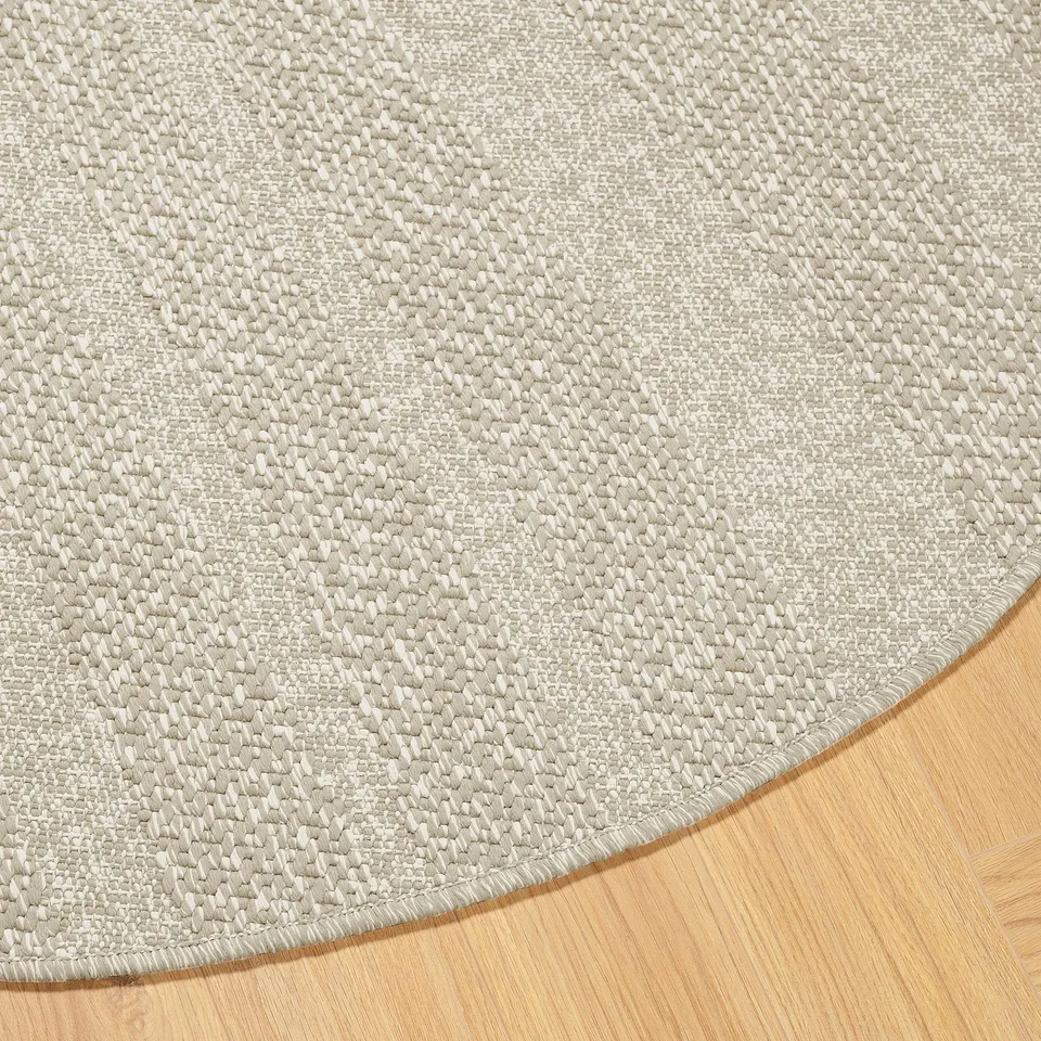 Round rug with textured beige pattern on hardwood floor, showcasing its intricate weave and smooth edges.