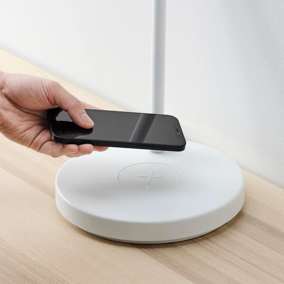Person placing smartphone on white wireless charging pad on wooden table.
