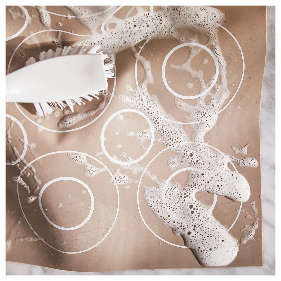 Brown BAKTRADITION silicone baking mat with circular patterns, white brush, and cleaning suds.