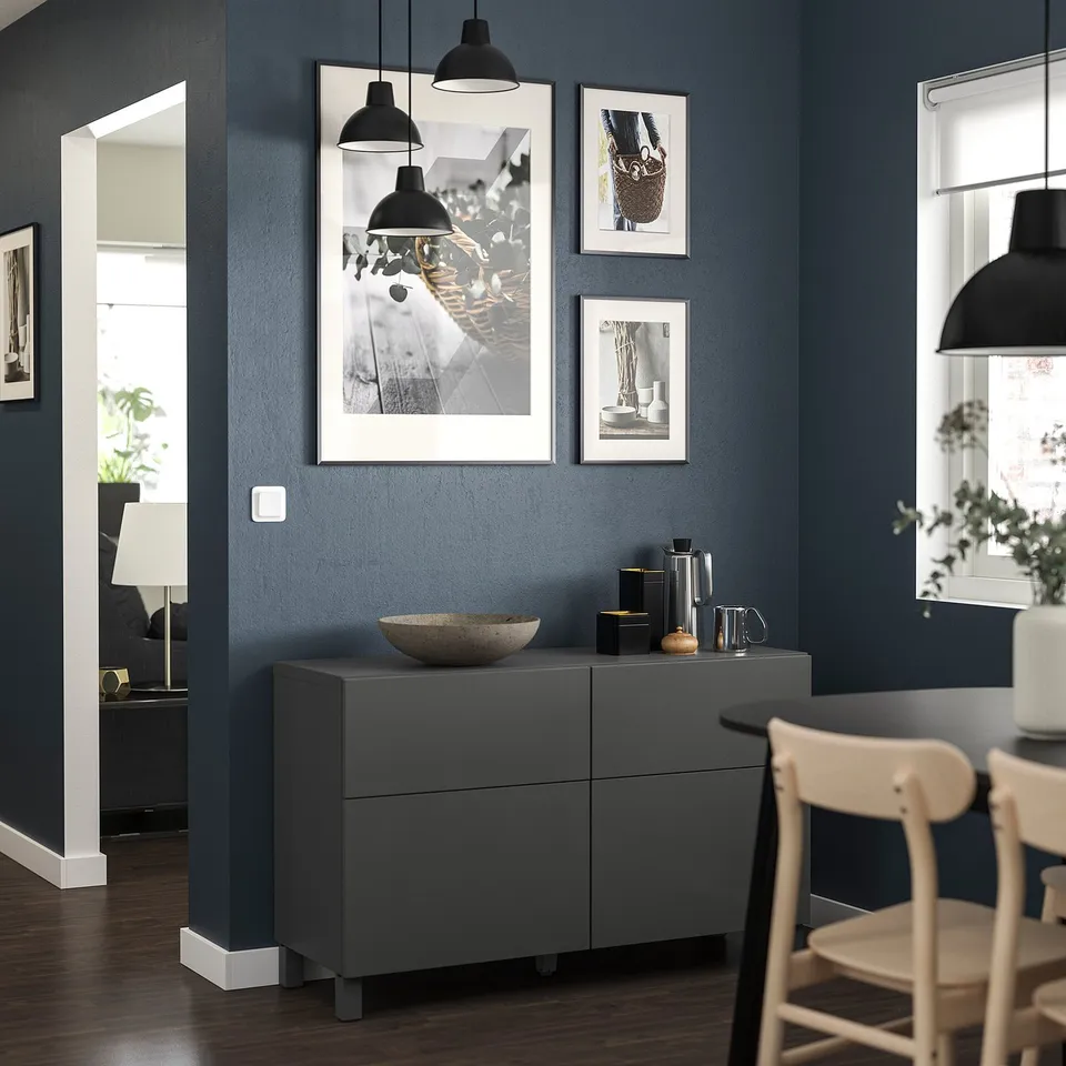 Modern living room with dark blue walls, grey BESTÅ unit, photos, & lights.