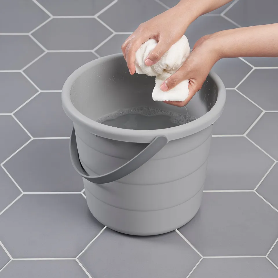 Person wrings out sponge over grey PEPPRIG bucket on tiled floor.