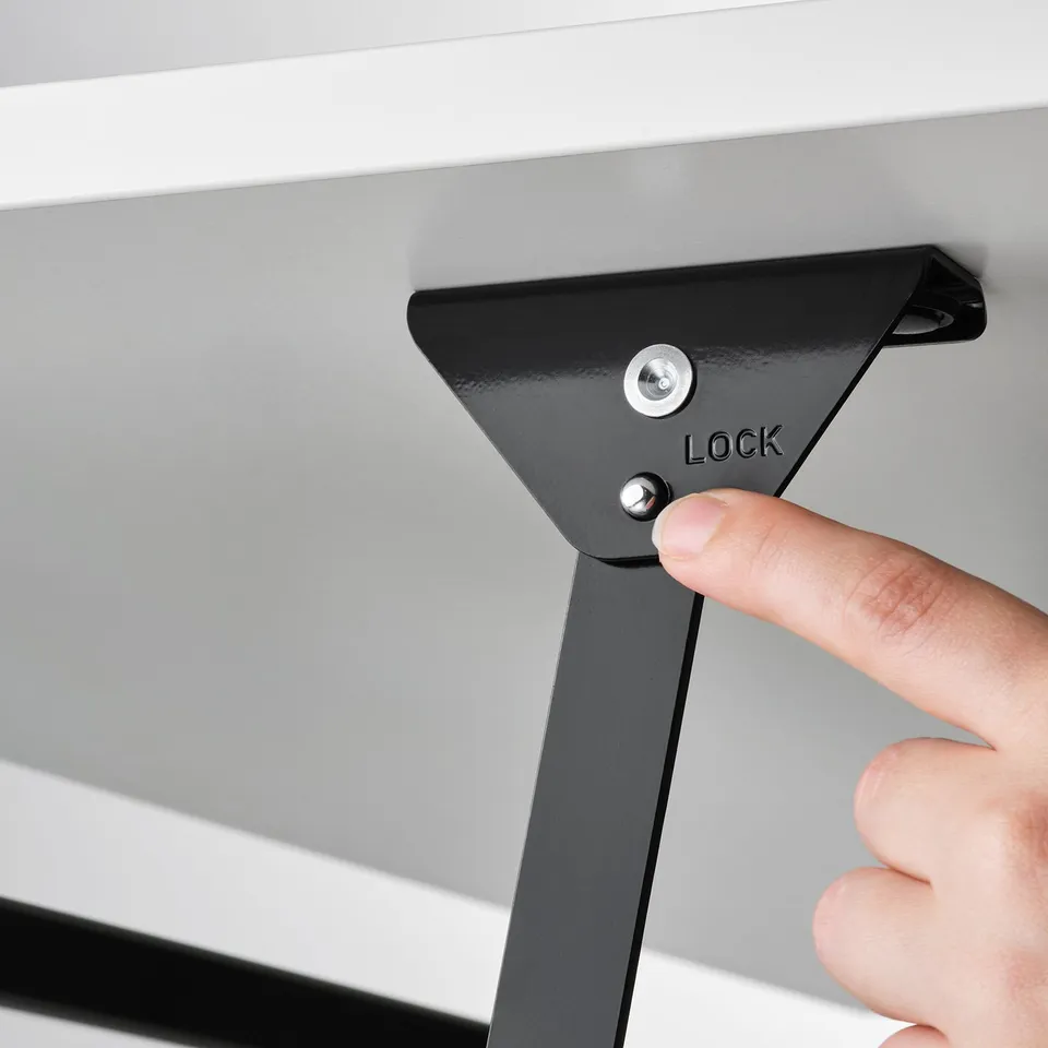 Hand pressing down black lock lever on adjustable coffee table; locks table in place.