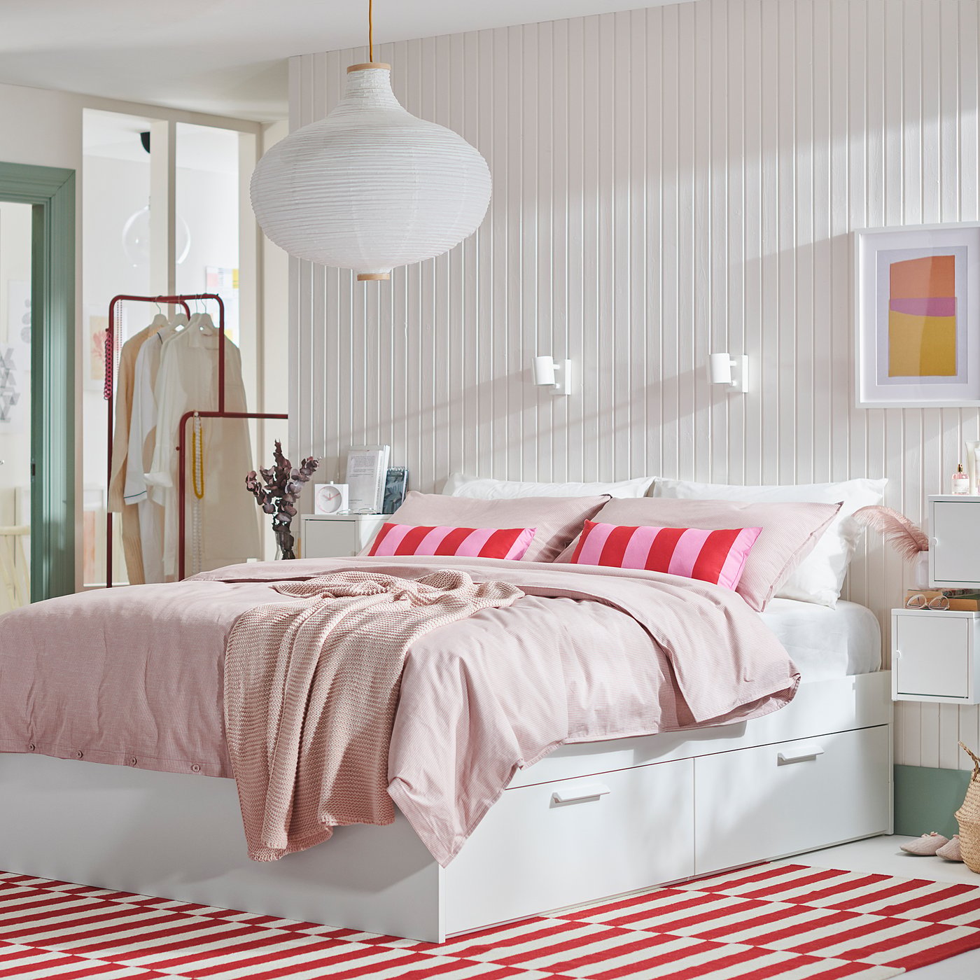 Bright, white modern bedroom featuring BRIMNES bed with four drawers, red striped rug, pink blankets, and a large white pendant light.