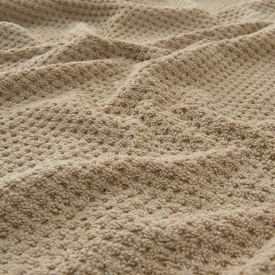 Soft, beige cotton towel with intricate, textured pattern, showcasing its fluffy and absorbent quality.