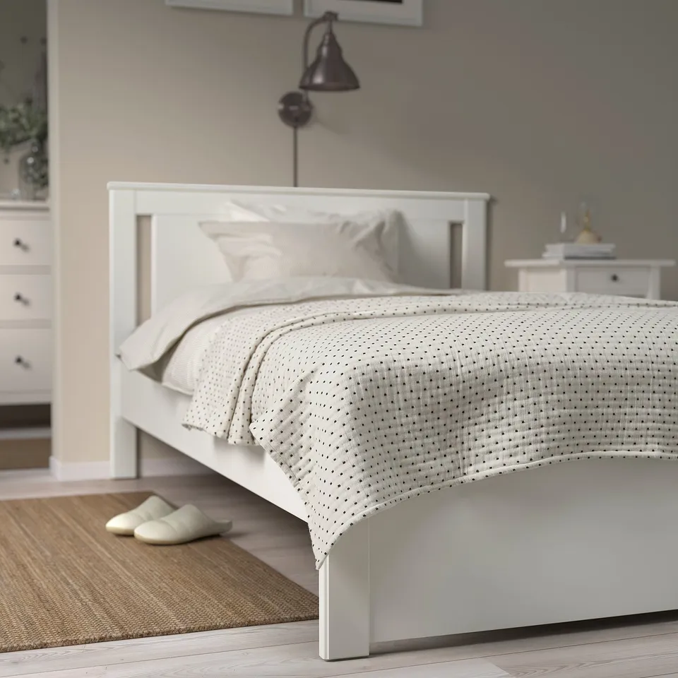 Bright bedroom with white JAKOBSLILJA bedspread, subtle grey stitching, neatly folded on large bed. Fits well with creamy slippers and rug.