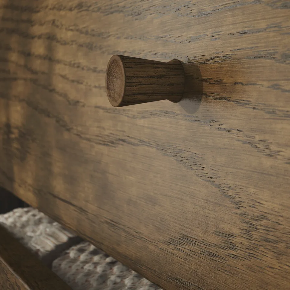 Small wooden drawer handle on a textured, light brown wooden surface. The handle has a smooth, rounded design, indicating quality craftsmanship.