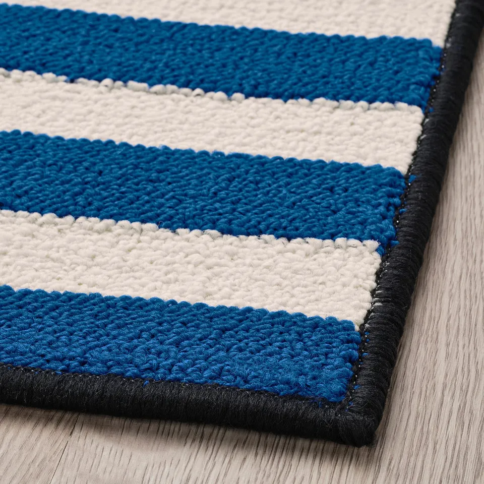 Blue and white striped rug with black border on light wooden floor, corner view.