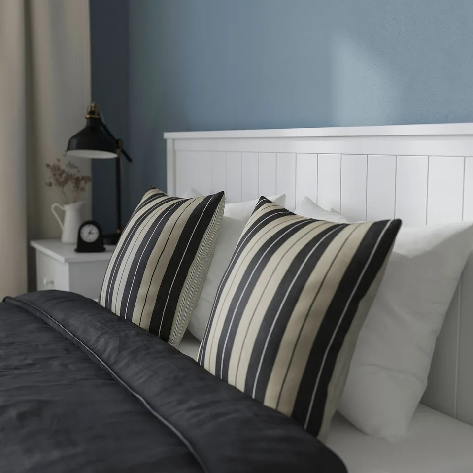 Bed with striped pillows and bedside table, showing sturdy design and headboard.