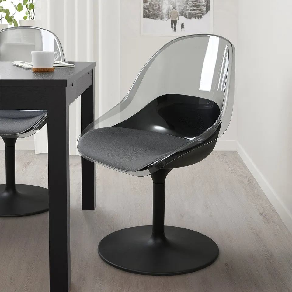 Black BALTSAR swivel chair with curved back and seat, near small table with white mug.
