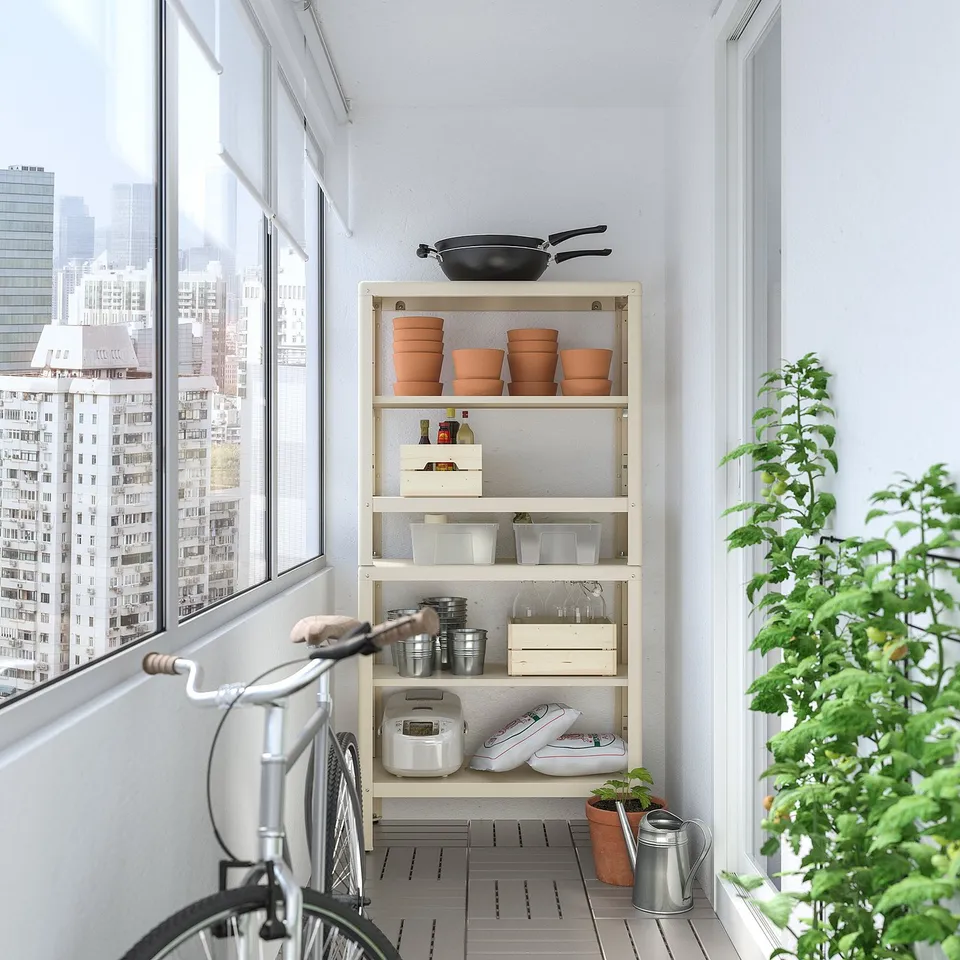 Balcony with white KOLBJÖRN shelving unit, holding pots and appliances. Black bicycle and green plant nearby. City view from window.