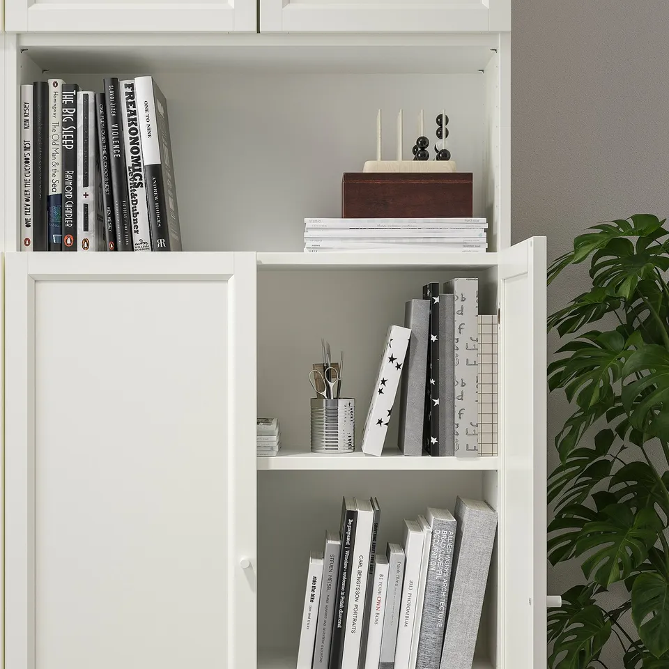 White bookcase with adjustable shelves and inset panel doors, storing various books and items.
