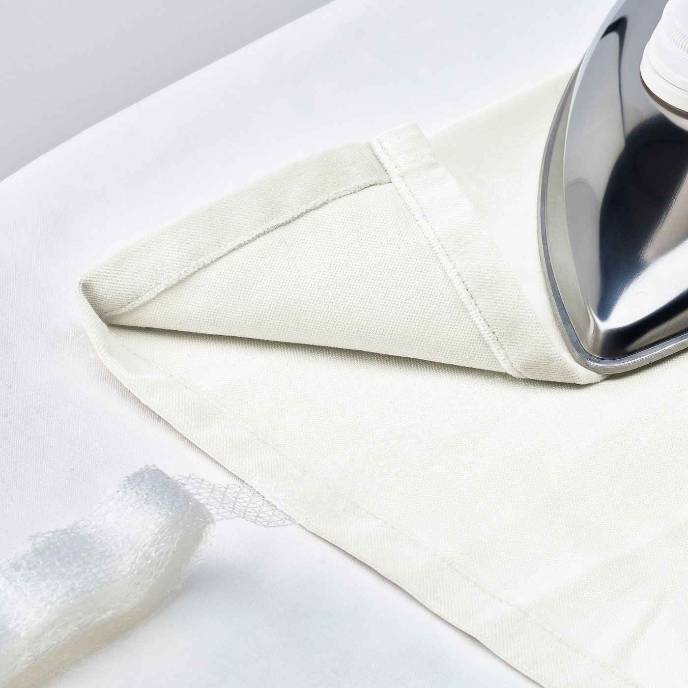 Folded white curtains on ironing board, ready for use. Silver iron beside them.