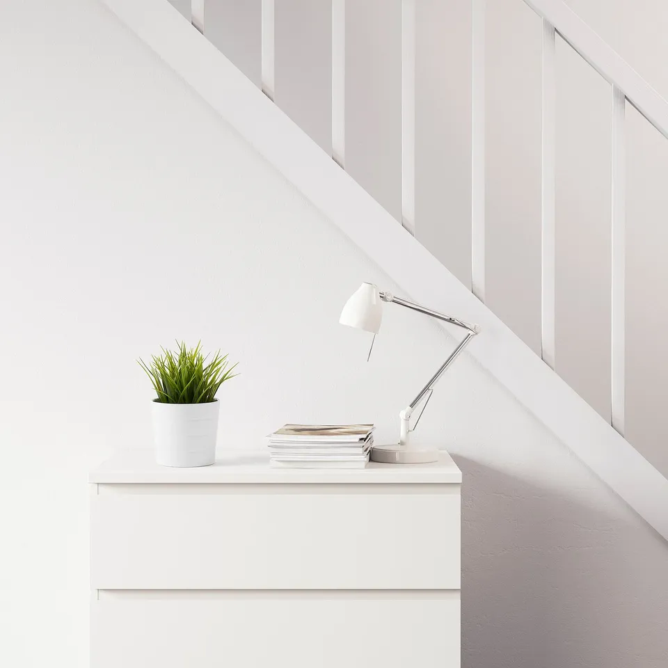White desk with lamp, books, and artificial plant.