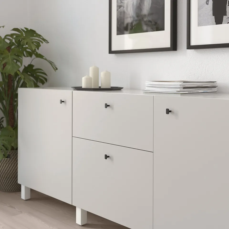 White cabinet with black knobs, 3 candles, plant, and wall art.