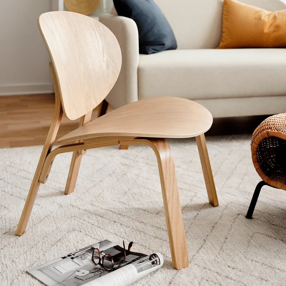 Light wooden chair with clean lines, natural finish, and curved seat on a white rug near a beige sofa.