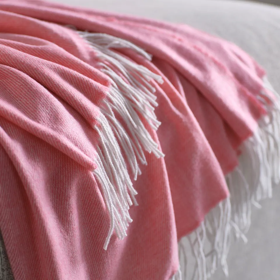 Soft pink throw blanket with fringes on edges, neatly folded, showcasing its cosy, recycled material quality.