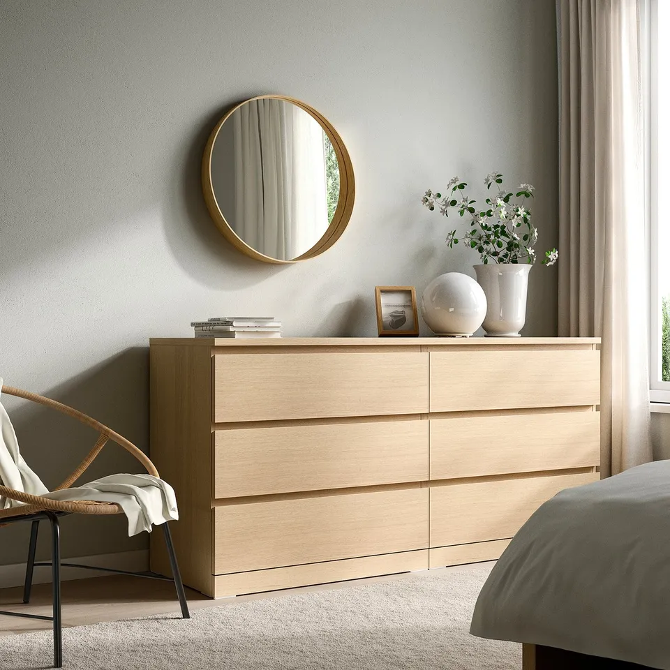 Minimalist bedroom with STOCKHOLM dresser, mirror, vase, candle, chair, and bed.