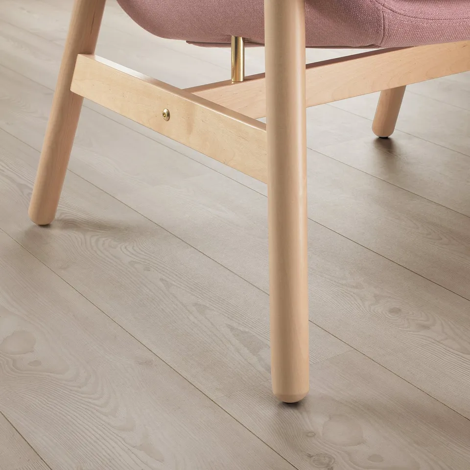 Modern chair on light wood floor. Curved back, light wood legs, pinkish seat cushion. Elegant and supportive design.