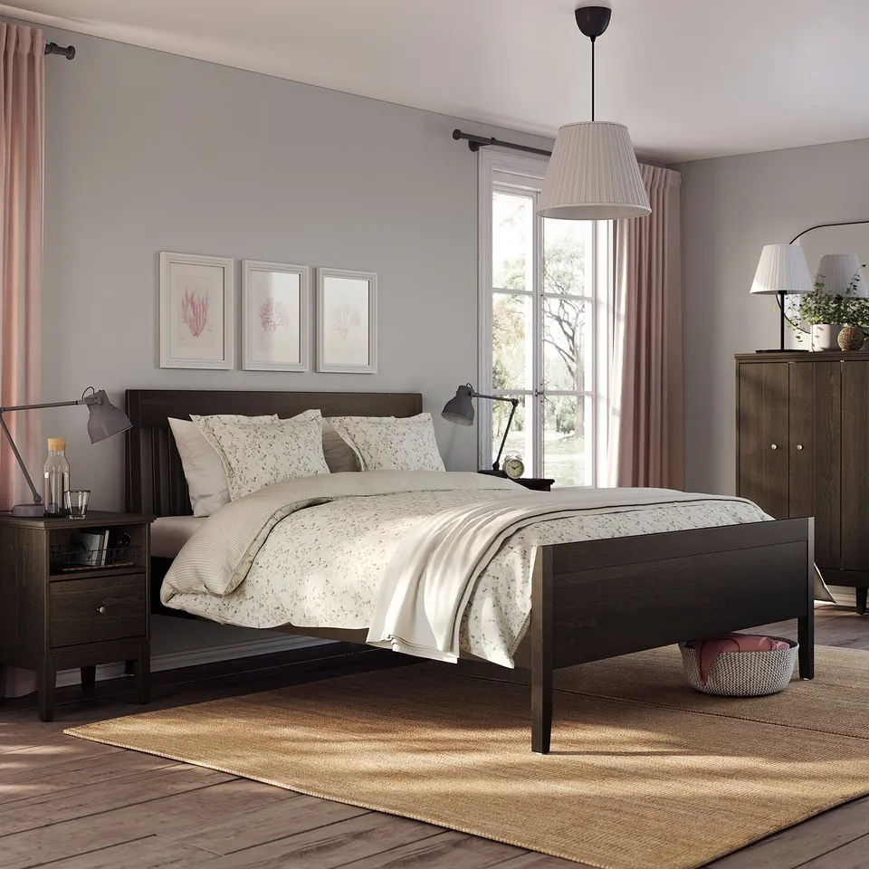 Modern bedroom with dark wood IDANÄS bed, light bedding, nightstands with lamps, large window, pink curtains, wooden dresser, and rug.