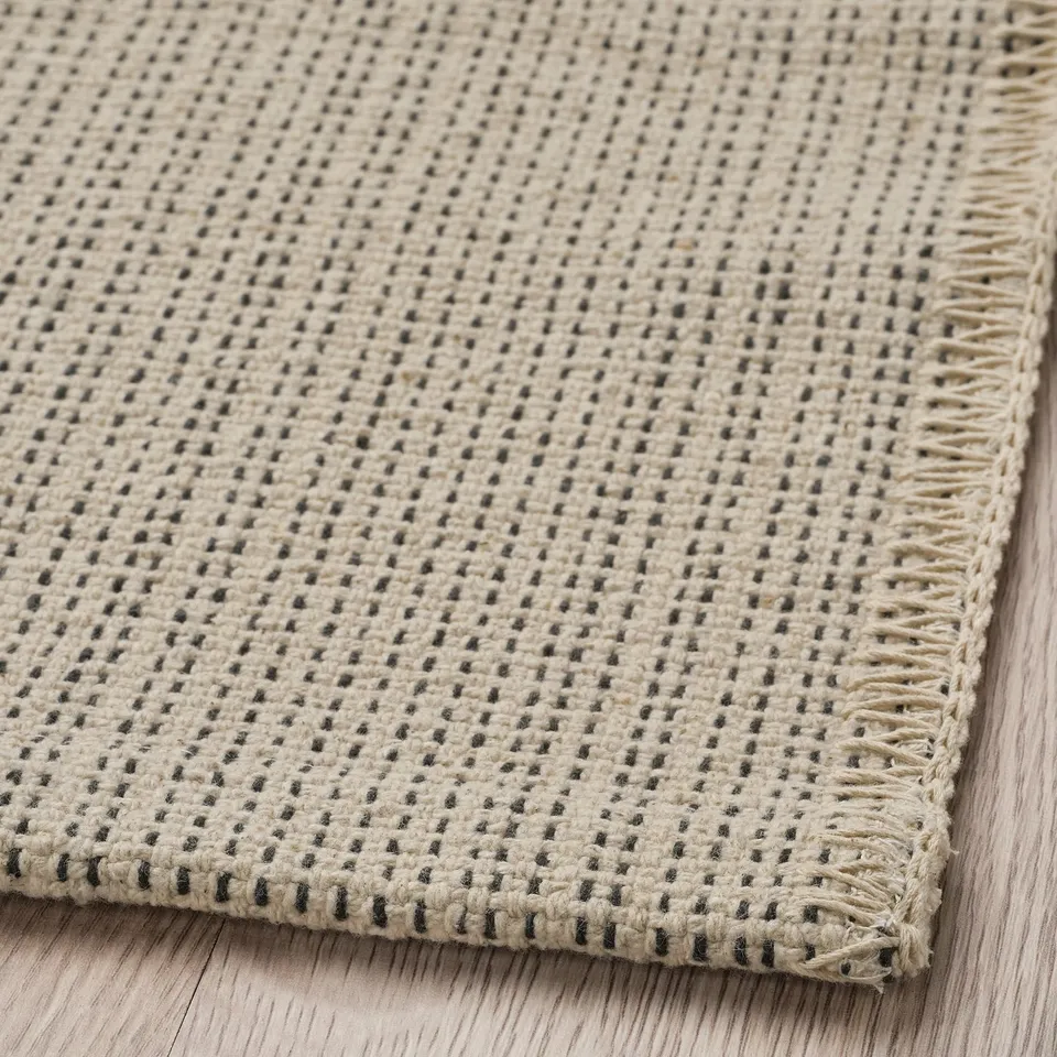 Img: soft, textured cotton rug, cream with black dots, neatly woven, laid on wood floor.