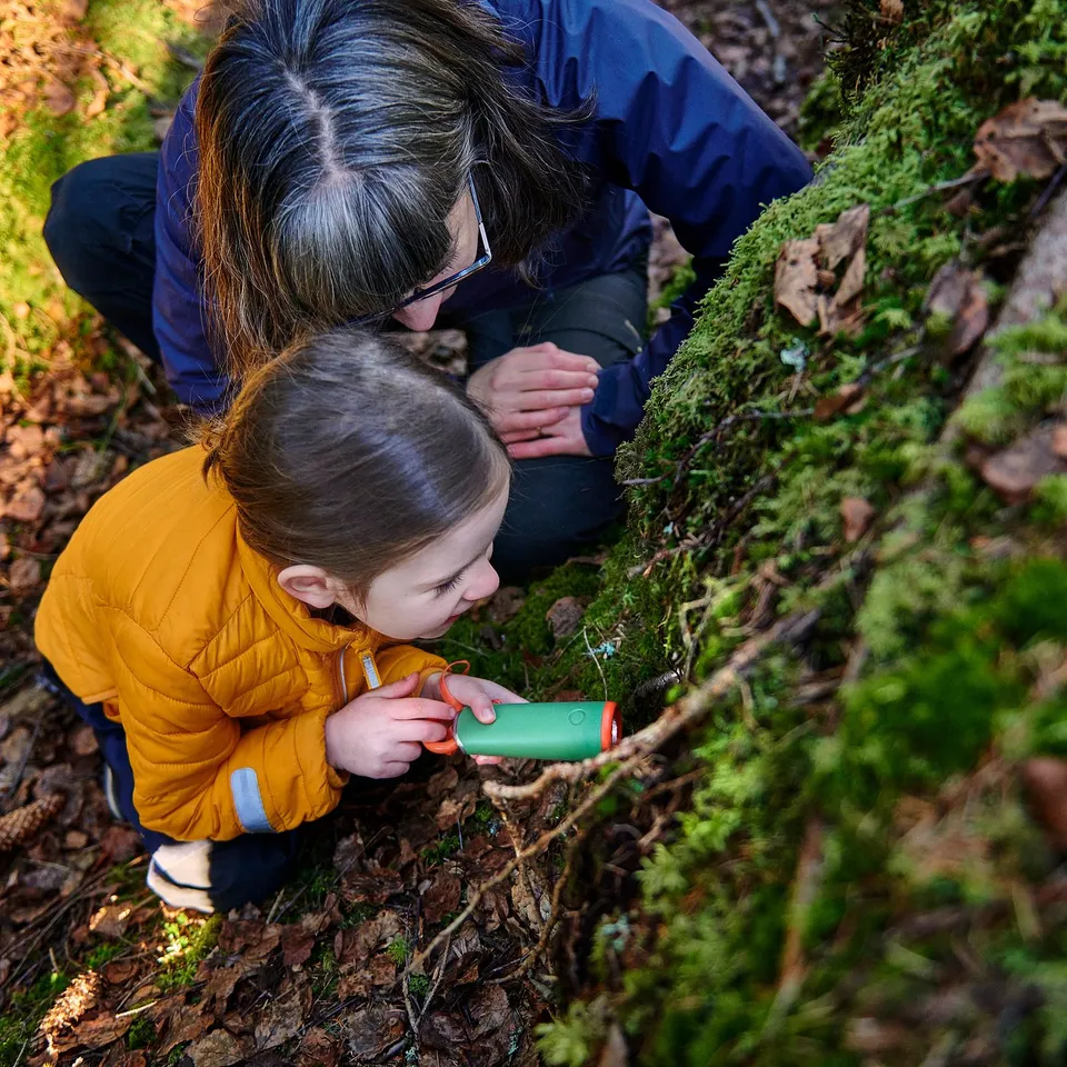 Two people, a child and an adult, explore moss on a log with a green torch.