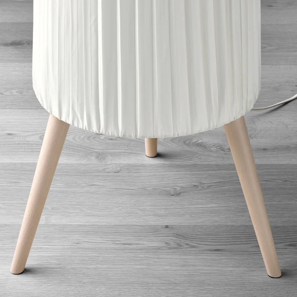 Modern floor lamp with pleated white shade, three wooden legs, diffused light.