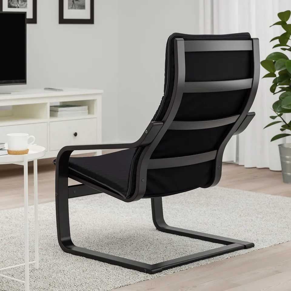 Black POÄNG armchair with curved lines, high back for neck support. Perfect for relaxation. On light rug, near white side table with coffee cup.