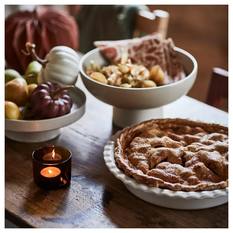 Wooden table with apple pie, candle, and pumpkins.