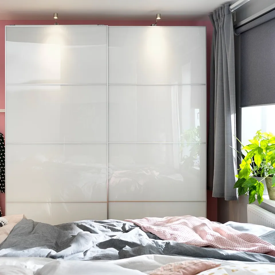 Large modern wardrobe with sleek white glass panels, shiny surface, sliding doors, and built-in lights.