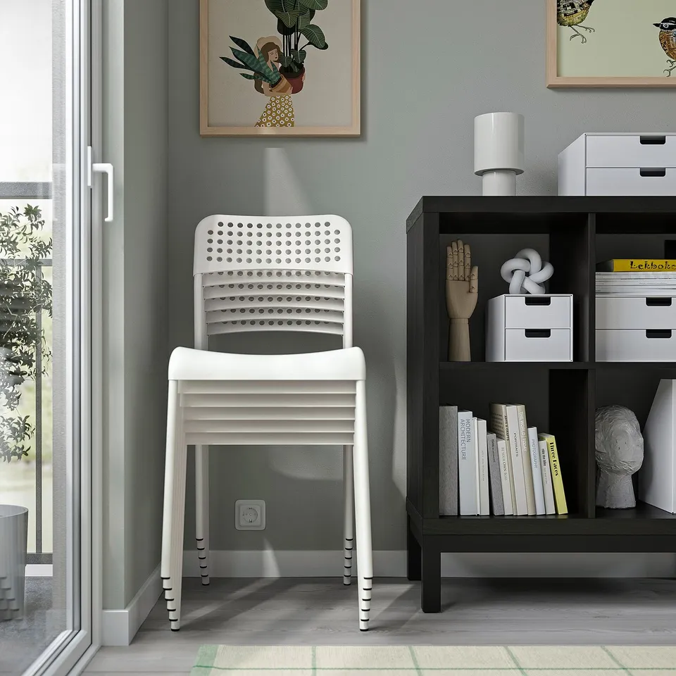 White plastic chair against wall, beside shelf with books, decorative items, light.