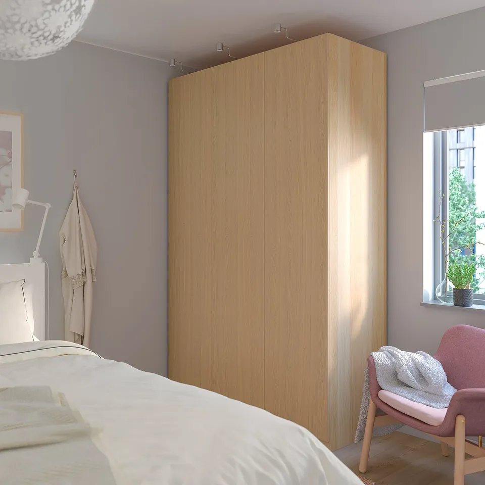 Modern bedroom with tall light wood PAX wardrobe between bed and window, minimalist design.