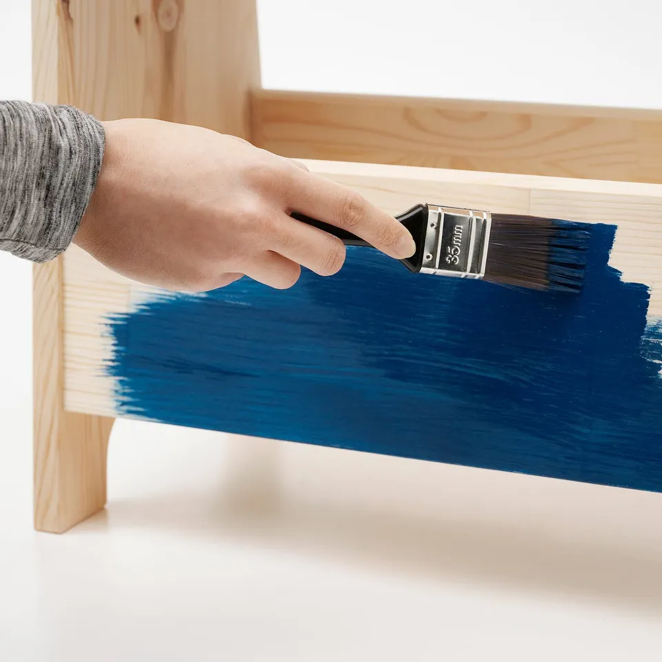 Hand painting wooden bench blue with 35mm brush, highlighting customization and indoor use.